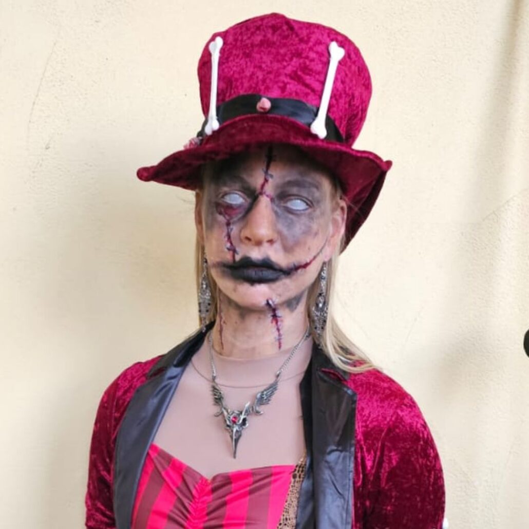 Voodoo pop-look met rode hoed en gestikte mond bij Halloween The Villains, gegrimeerd door SchminkenGrime.nl, verkrijgbaar bij SchminkenGrime.nl