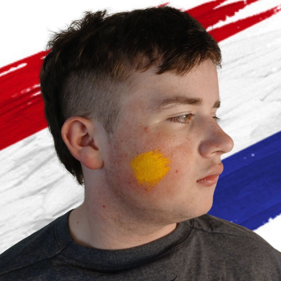 Gele basis van een eenvoudig Koningsdag leeuwtje schminken op de wang verkrijgbaar bij SchminkenGrime.nl