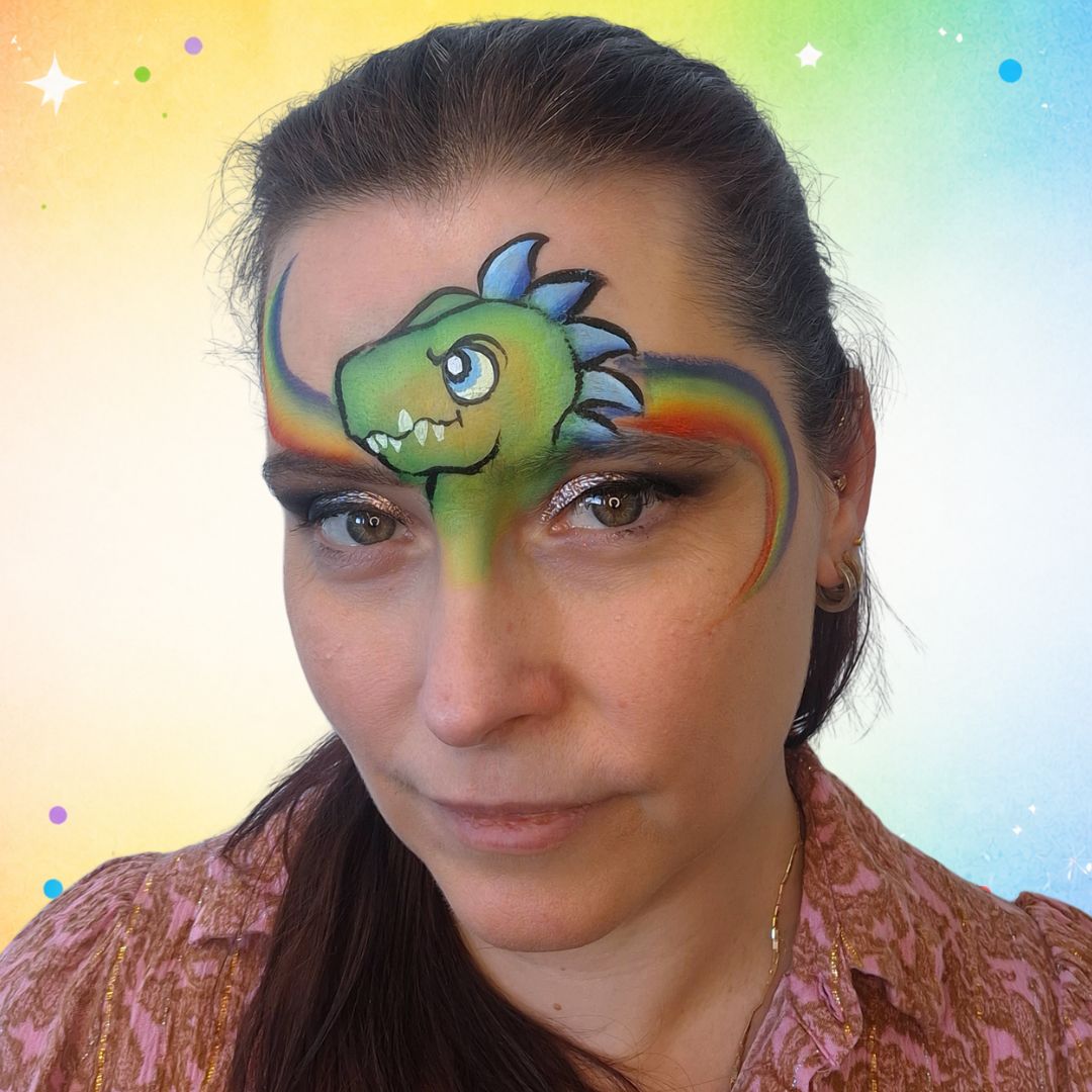 Regenboog achtergrond met Flabbergasted regenboog-splitcake getrokken in vloeiende boog achter de dino-kop met FBFX Simone schuin penseel 5/8, verkrijgbaar bij SchminkenGrime.nl