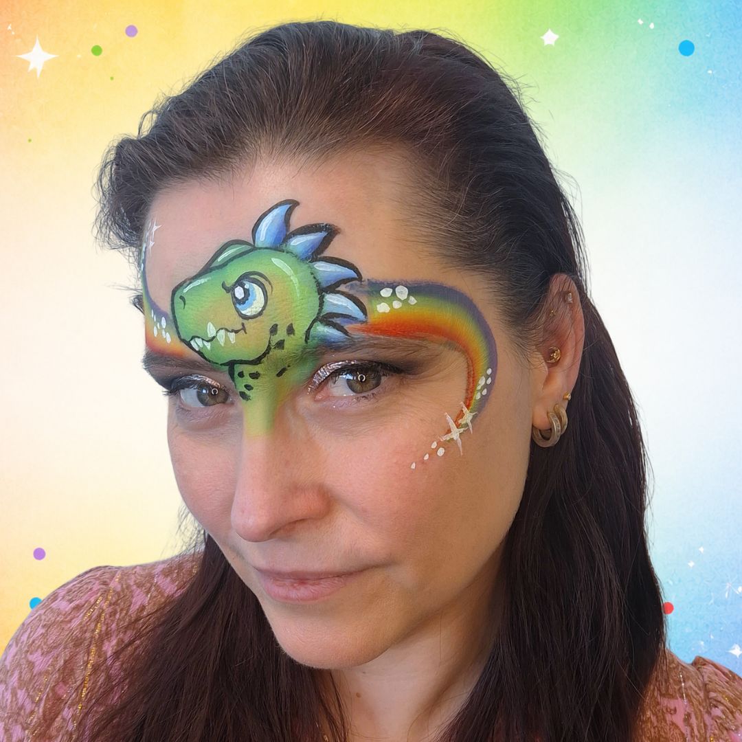 Afgewerkte dino schminklook met witte sterretjes, stippen, glitter en highlights langs de regenboog en op de wang, verkrijgbaar bij SchminkenGrime.nl