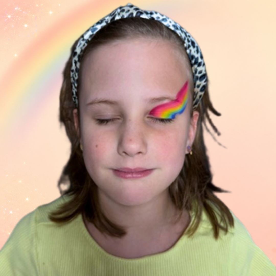 Stap 1 van de regenboog schminken: twee schuine regenbogen aangebracht met de DFX Bright Rainbow splitcake en het FBFX Simone 1 inch penseel, eentje vanaf de wimperrand schuin omhoog en eentje hoger op het voorhoofd, verkrijgbaar bij SchminkenGrime.nl.