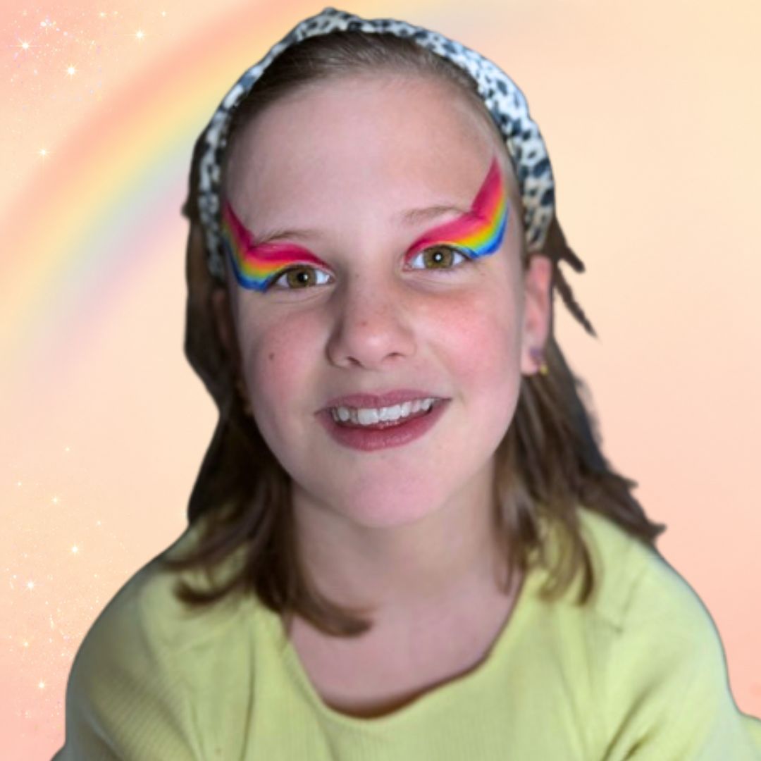 Stap 2 van de regenboog schminken: witte bloem met cerise rode accenten in het midden tussen de twee regenbogen, gemaakt met een dubbel geladen FBFX Eva 2 penseel, verkrijgbaar bij SchminkenGrime.nl.