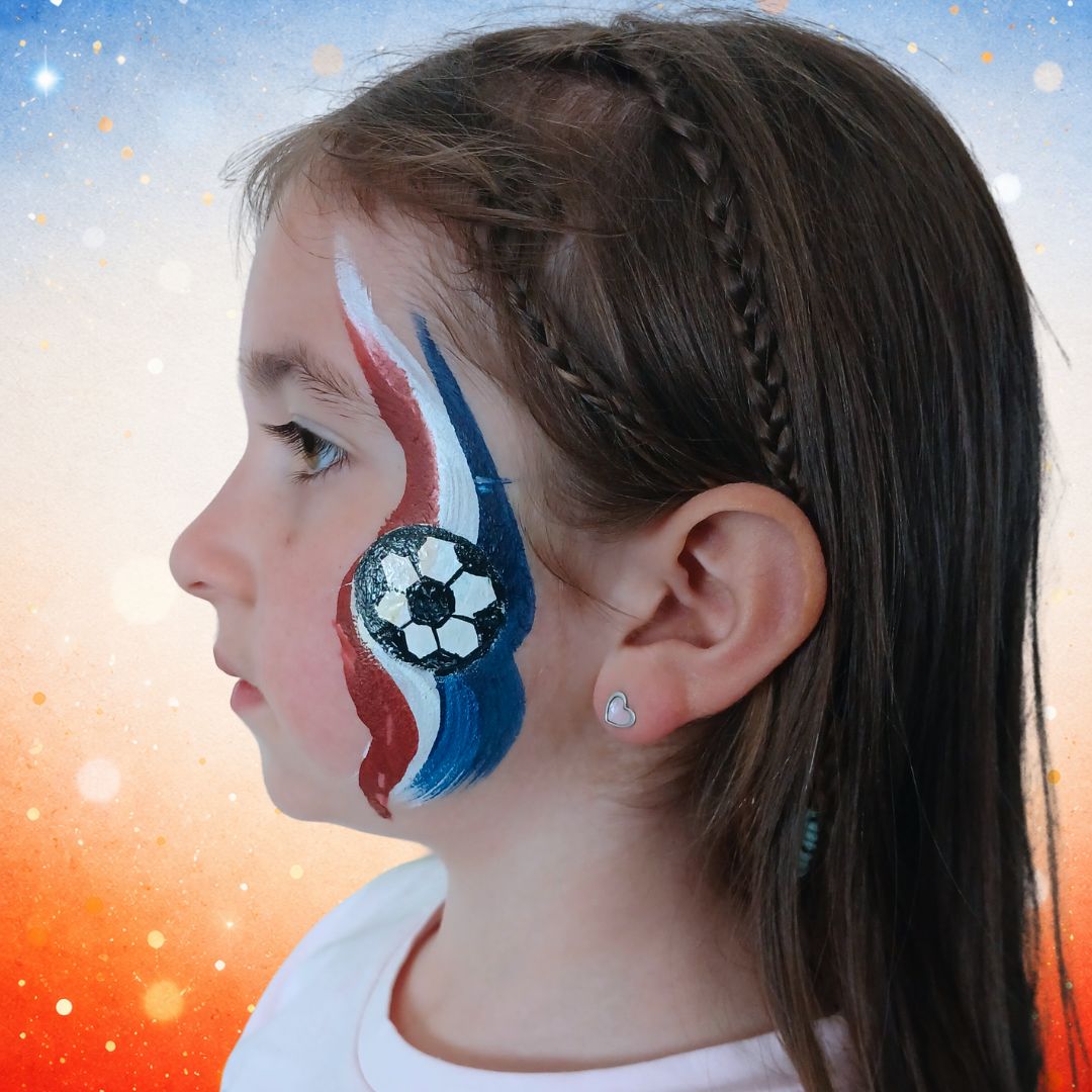 Oranje en witte bloemmetjes en stipjes als afwerking rondom de voetbal en op de rood-wit-blauwe veeg, met FBFX Eva 1 en Superstar Maayke 12 penselen, verkrijgbaar bij SchminkenGrime.nl.