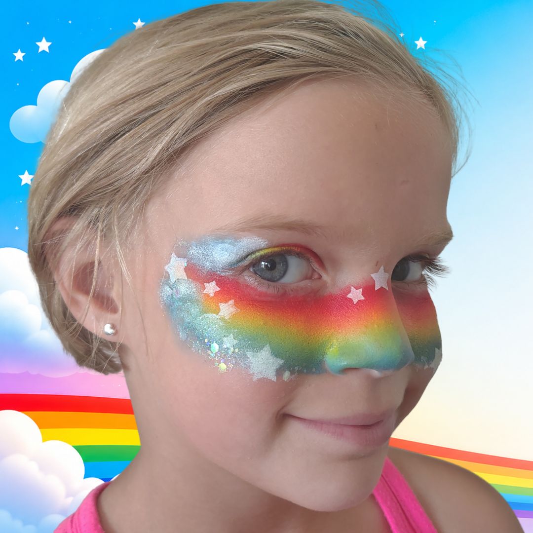 Afgewerkte cheek art regenboog met chunky glitter over de witte wolkjes op een lachend kind, verkrijgbaar bij SchminkenGrime.nl