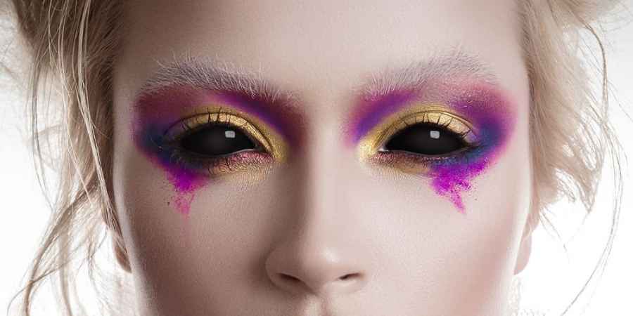 Close-up van ogen met volledig zwarte kleurlenzen en felroze, paarse en gouden oogmake-up