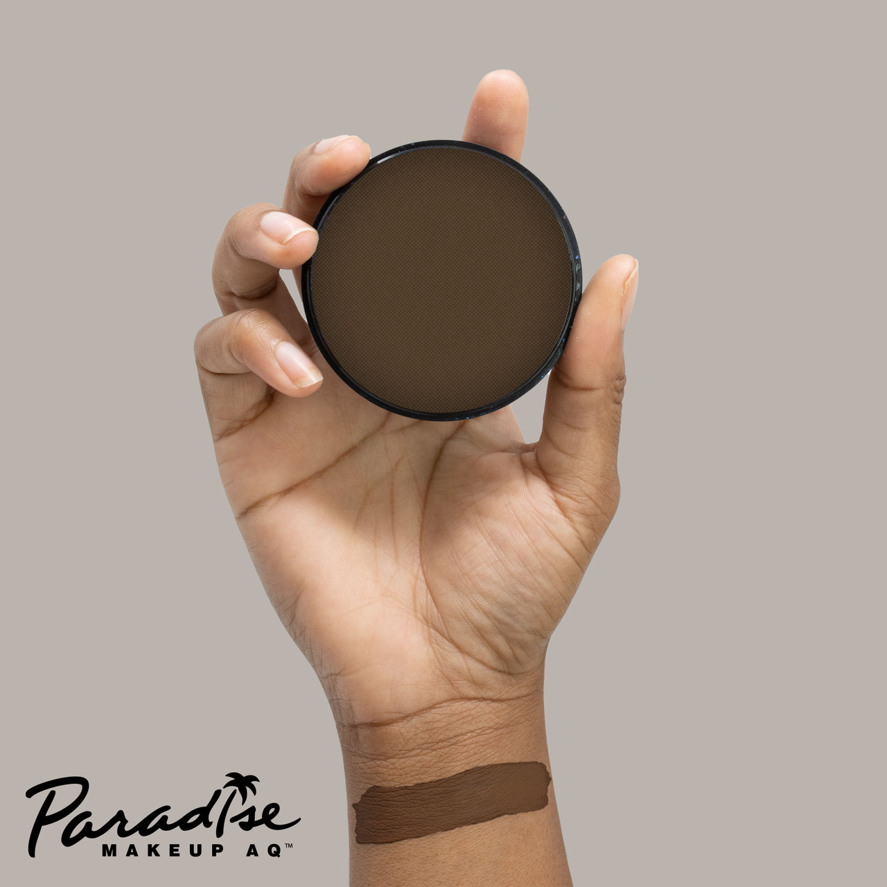 Mehron Paradise Dark Brown 40gr – bruine schmink op hand, verkrijgbaar bij SchminkenGrime.nl Mehron Paradise Makeup Dark Brown 40 gram op hand aangebracht met verpakking erbij, toont pigmentatie en dekking van de professionele bruine waterschmink, verkrijgbaar bij SchminkenGrime.nl